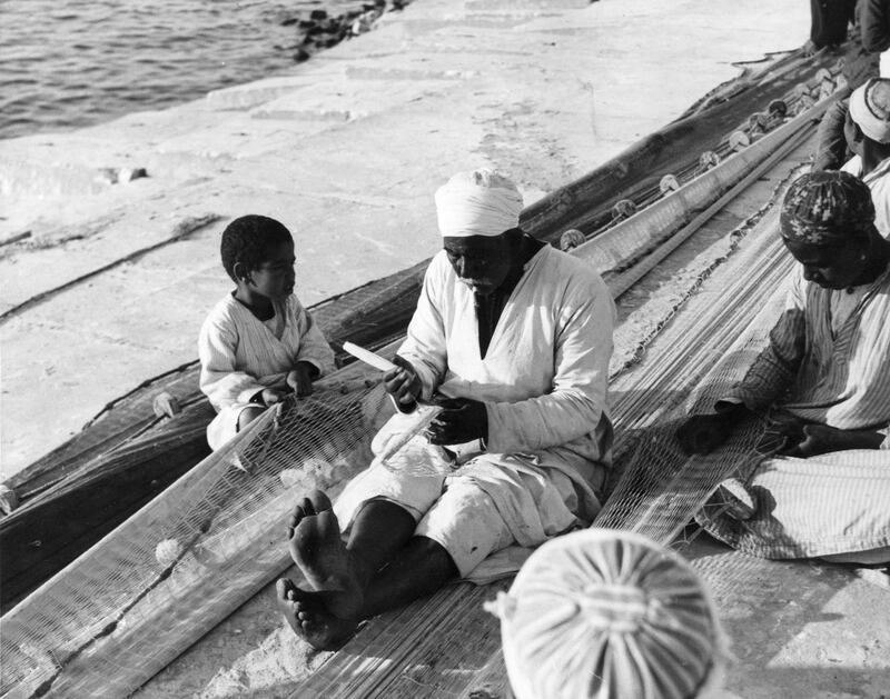 5th August 1948:  A young boy watches as his father mends fishing nets on the seashore in Egypt.  (Photo by Fox Photos/Getty Images)