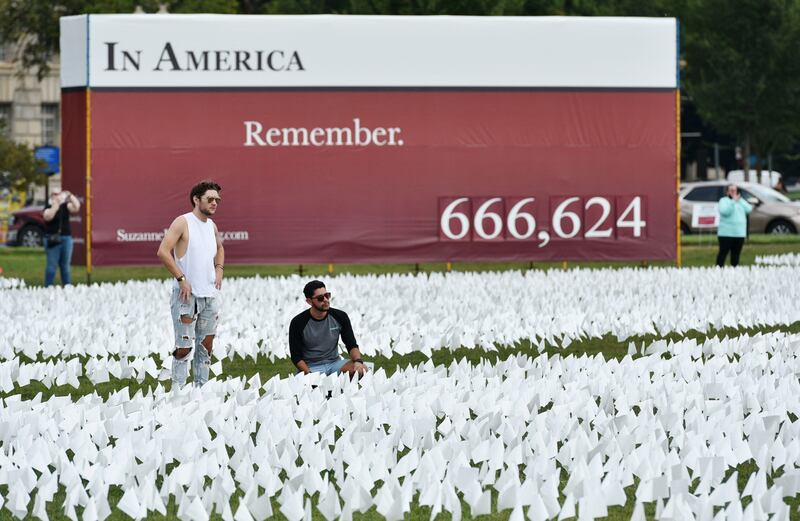 Men are seen in a field of white flags on the Mall near the Washington Monument in Washington, DC on September 16, 2021.  - The project, by artist Suzanne Brennan Firstenberg, uses over 600,00 miniature white flags to symbolize the lives lost to Covid-19 in the US.  (Photo by MANDEL NGAN  /  AFP)