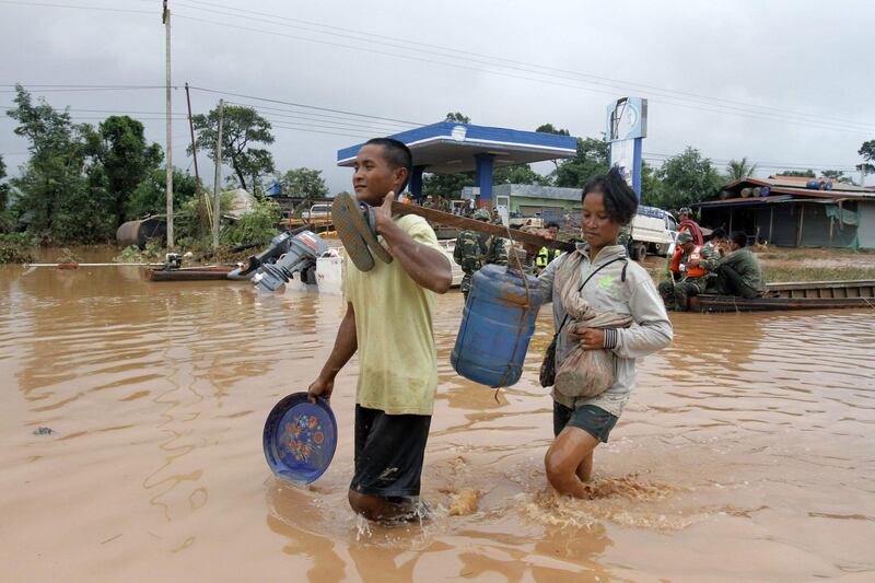 Victims wade through a flooded street as they carry drinking water in Sanamxai, Attapeu province. AFP