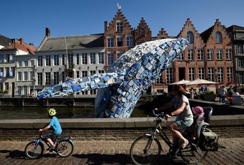 People ride past a 10-metre installation depicting a whale, made up of five tons of plastic waste pulled out of the Pacific Ocean, displayed in Brugges. AFP