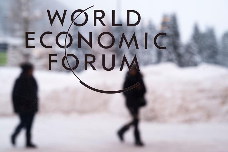 Two persons walk behind the logo of the World Economic Forum at the meeting's conference center in Davos, Switzerland, Sunday, Jan. 21, 2018. One question looms as President Donald Trump packs his bags and heads for the mountains of Switzerland later this week: How will the diet Coke-loving nationalist fit in with the champagne-swilling globalists heâ€™ll encounter at the World Economic Forum in Davos?  (AP Photo/Markus Schreiber)