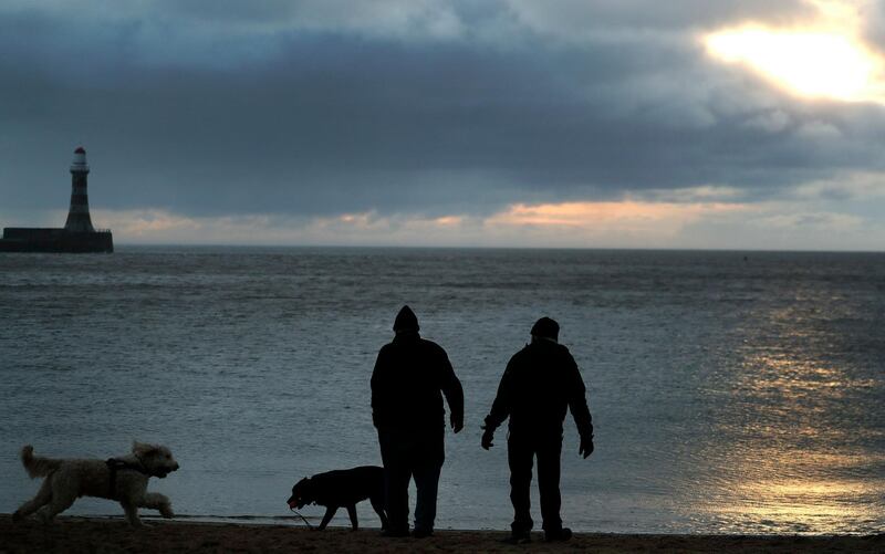 Men walk their dogs as the sun rises at Roker beach in Sunderland, England, Friday, March 15, 2019. Sunderland voted for Brexit to make itself heard, and in hope of a brighter future. This city in northeast England once built ships that drove global commerce and helped Britain rule the waves. Coal from the surrounding mines helped power the country.(AP Photo/Frank Augstein)