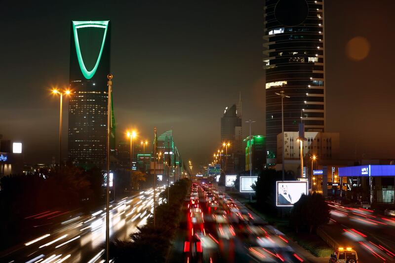 In this picture taken with a slow shutter speed, vehicles pass in front of the landmark Kingdom Tower, at left, as it projects a green light marking Saudi 89th National Day celebrations in Riyadh, Saudi Arabia, late Sunday, Sept. 22, 2019. (AP Photo/Amr Nabil)