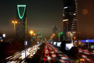In this picture taken with a slow shutter speed, vehicles pass in front of the landmark Kingdom Tower, at left, as it projects a green light marking Saudi 89th National Day celebrations in Riyadh, Saudi Arabia, late Sunday, Sept. 22, 2019. (AP Photo/Amr Nabil)