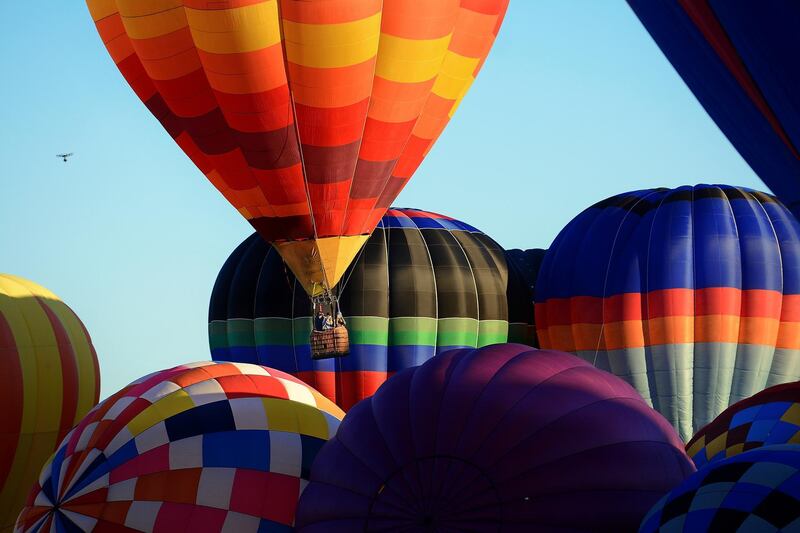 A hot air balloon lifts off between other balloons still inflating. AP Photo