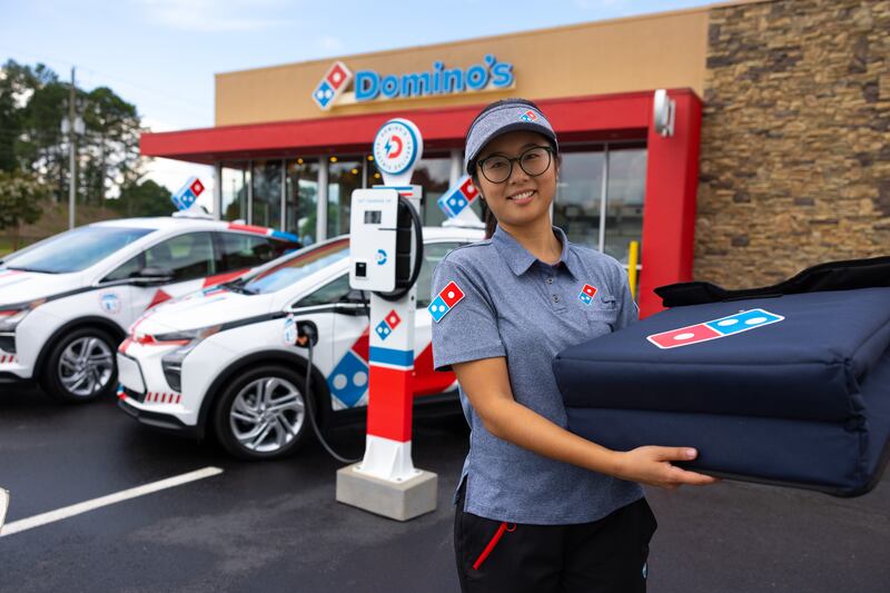A Domino's delivery driver next to the company's new vehicles.