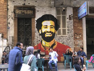 A picture taken on April 4, 2018 shows people sitting at a cafe in downtown Cairo with a mural depicting Liverpool FC's Egyptian striker Mohamed Salah painted in the background. / AFP PHOTO / Amir MAKAR