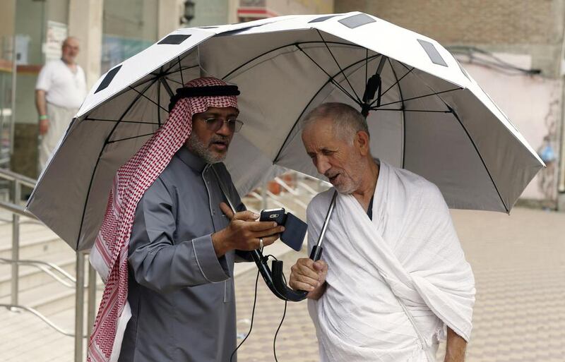 Saudi engineer Kamel Badawi, left, shows off his invention, the smart umbrella in the Saudi holy city of Mecca, on September 8, 2016. The umbrella uses solar energy to cool the user. AHMAD GHARABLI  / AFP