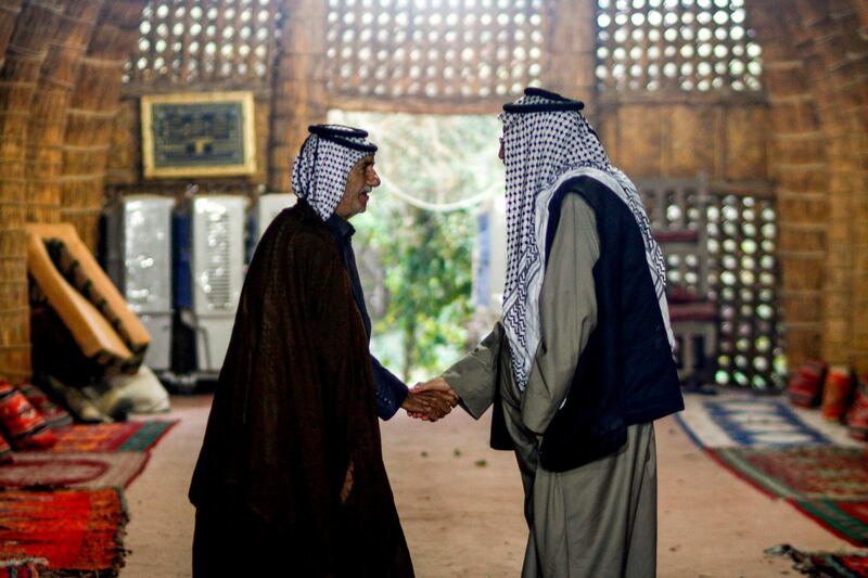 Members of an Iraqi clan shake hands as they meet inside a straw tent in the town of Mishkhab, south of Najaf on November 15, 2018. For centuries, Iraqi clans have used their own system to resolve disputes, with tribal dignitaries bringing together opposing sides to mediate in de facto "hearings" and if one side failed to attend the rival clan would fire on the absentee's home their fellow tribesmen's, a practice known as the "degga ashairiya" or "tribal warning". 
Authorities however are currently classifying it as a "terrorist act" punishable by death. / AFP / Haidar HAMDANI
