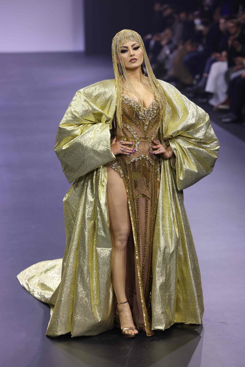 Bollywood actress Urvashi Rautela wore a floor-sweeping beaded gown featuring a thigh high slit, an oversized gold lame cape with statement sleeves flung over her shoulders and a chainmail headpiece which added to the overall indulgence.