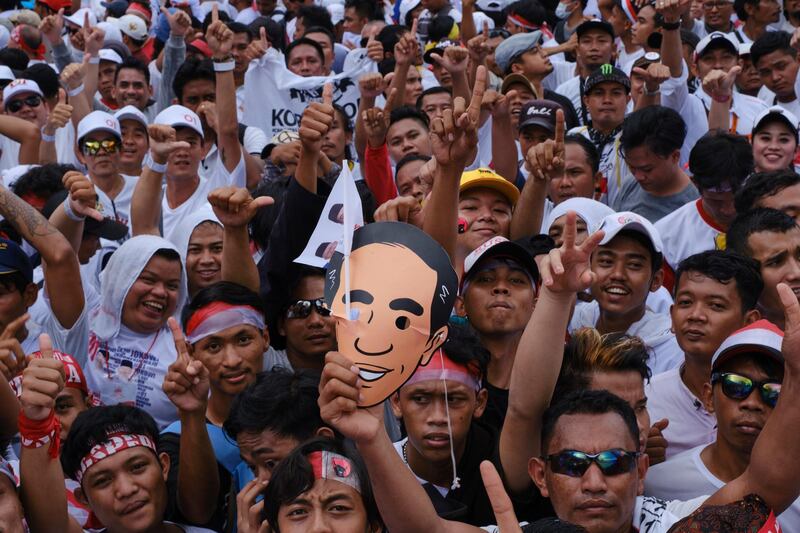 A crowd holding a a mask with a cartoon image of Indonesian President Joko Widodo during a rally at Jakarta's main stadium on April 13, 2019. Getty Images