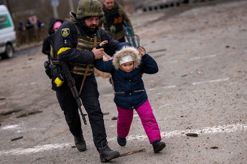 A Ukrainian police officer runs with a child as the sound of shelling echoes nearby in Irpin. AP