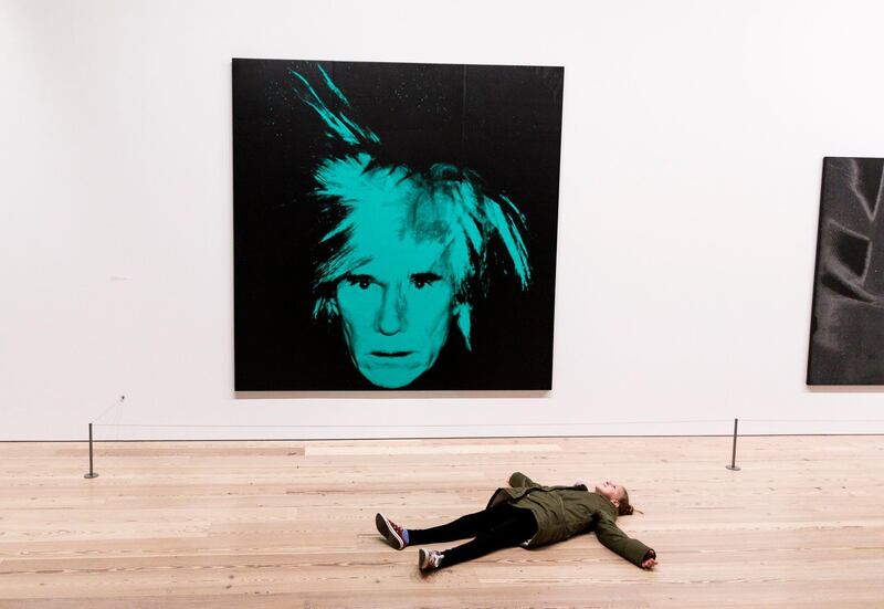 A girl lies on the floor near a self portrait of Andy Warhol at the show 'Andy Warhol - From A to B and Back Again' at the Whitney Museum of American Art in New York, US. EPA