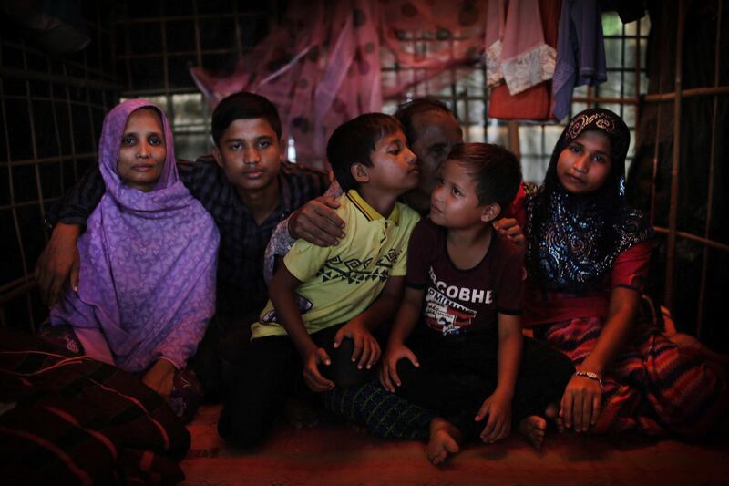 In this Nov. 25, 2017, photo, Bodru Duza, 52, third from right, kisses his sons as he sits for a portrait with members of his family in a tent in Kutupalong refugee camp in Bangladesh. After a massacre on their, Duza lost track of his wife and children and fled to Bangladesh alone, assuming all of them had been killed. But in mid-November, they were reunited in a refugee camp in Bangladesh. More than 650,000 Rohingya Muslims have fled to Bangladesh from Myanmar since August, and many have brought with them stories of atrocities committed by security forces in Myanmar, including an Aug. 27 army massacre that reportedly took place in the village of Maung Nu. (AP Photo/Wong Maye-E)