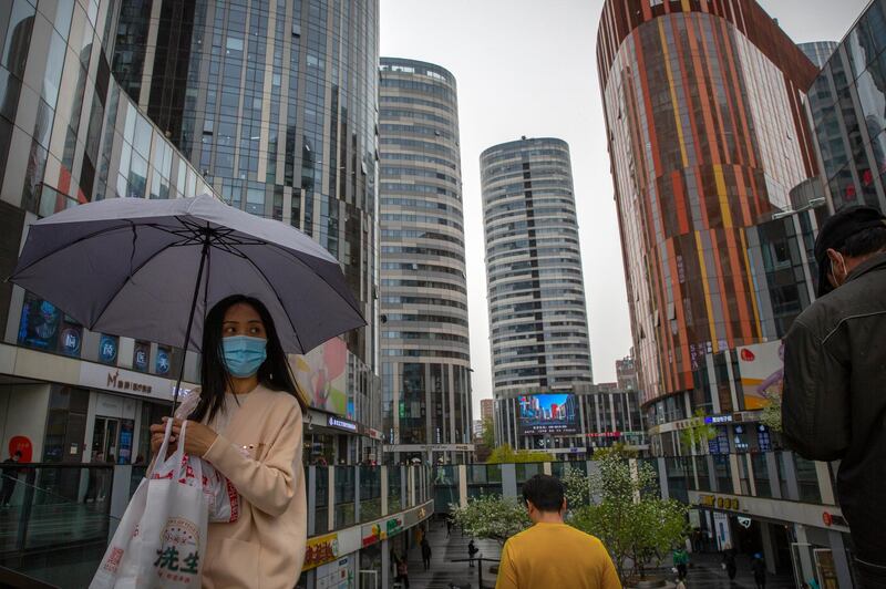 A woman wearing a face mask to help protect against COVID-19 walks through an office and shopping complex on a rainy day in Beijing. A Chinese border city hit by a fresh outbreak of COVID-19 this week began a five-day drive Friday to vaccinate its entire population of 300,000 people.  AP Photo