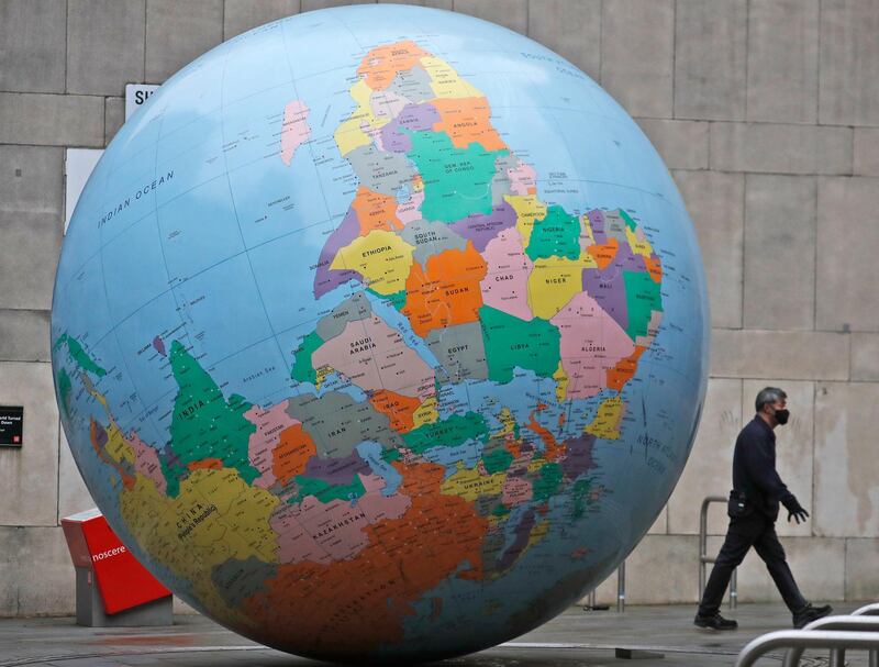 A man wearing a face mask walks past a globe in front of the London School of Economics in London. AP Photo