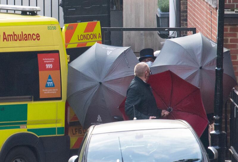 Staff shield the exit with umbrellas alongside an ambulance outside the rear of the King Edward VII Hospital in London. AP Photo