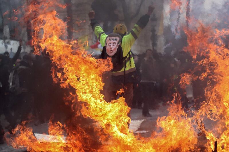 A yellow-vest protester wears a mask depicting French President Emmanuel Macron on which is written 'psycho'. AFP