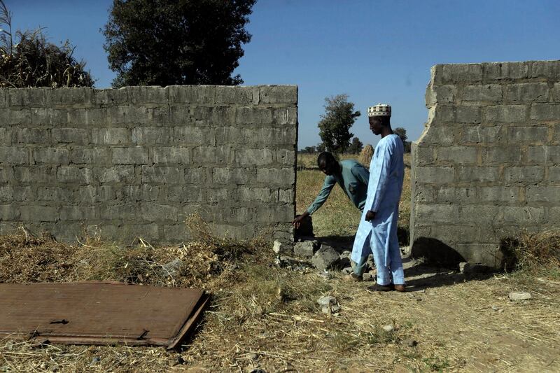 People inspect a wall and metal door broken by Boko Haram. AP Photo
