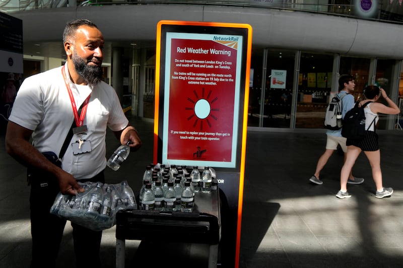 A railway worker hands out bottles of water to passengers at London's King's Cross, where there are train cancellations due to the heat. AP