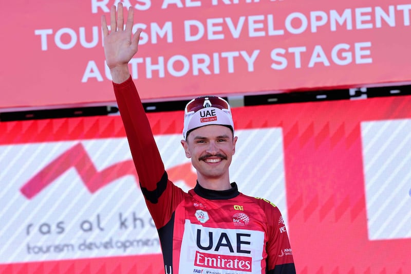 UAE Team Emirates rider Jay Vine celebrates on the podium in his leader's red jersey.