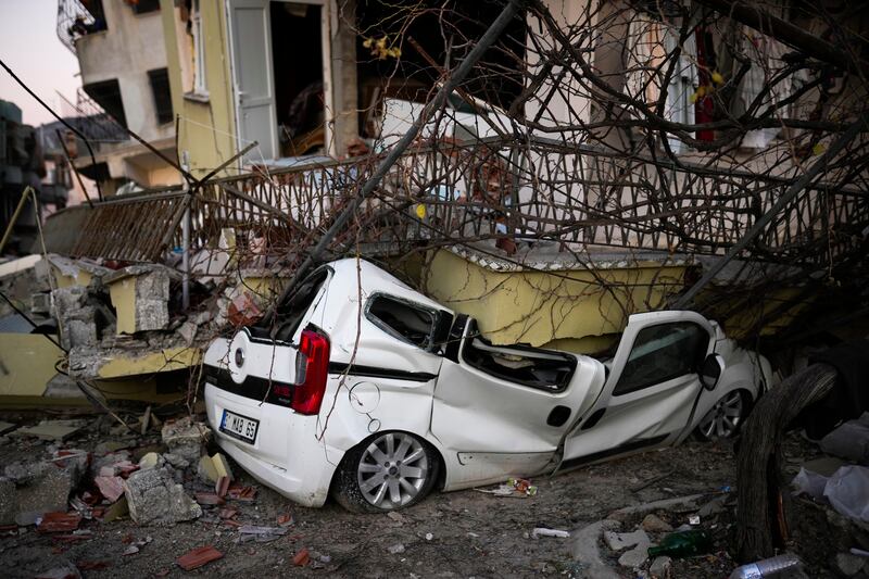 A car lies crushed by parts of a badly damaged building in Samandag, Turkey. AP