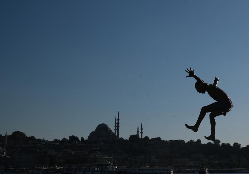 A young boy jumps from Galata Bridge  into the Bosphorus to cool off during warm weather while background seen Suleymaniye Mosque, amid the ongoing coronavirus pandemic in Istanbul.  EPA