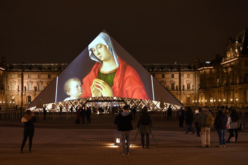 People take photos of the Louvre Pyramid in Paris as images of art on display at the Louvre Abu Dhabi are projected onto the landmark. Eric Feferberg / AFP