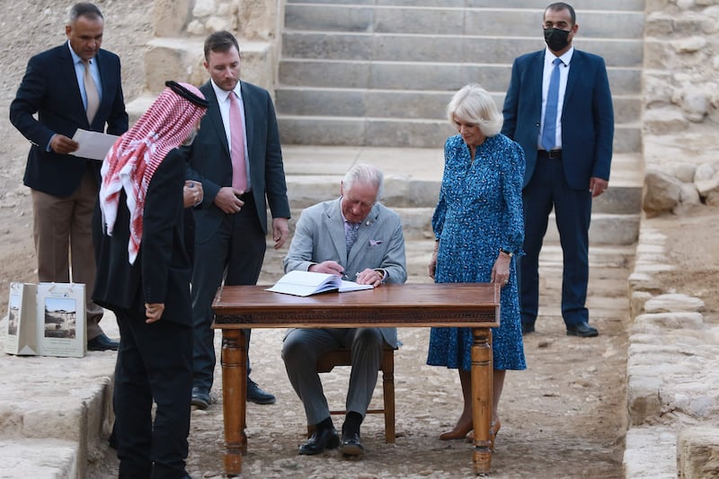 Prince Charles writes in a visitor book during his visit to Al Maghtas as the Duchess of Cornwall looks on. AFP