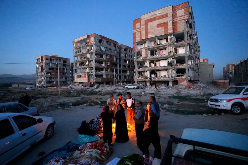 In this photo provided by the Iranian Students News Agency, ISNA, survivors of the earthquake warm themselves in front of destroyed buildings at the city of Sarpol-e-Zahab in western Iran, Monday, Nov. 13, 2017. A powerful earthquake shook the Iran-Iraq border late Sunday, killing more than one hundred people and injuring some 800 in the mountainous region of Iran alone, state media there said. (Pouria Pakizeh/ISNA via AP)
