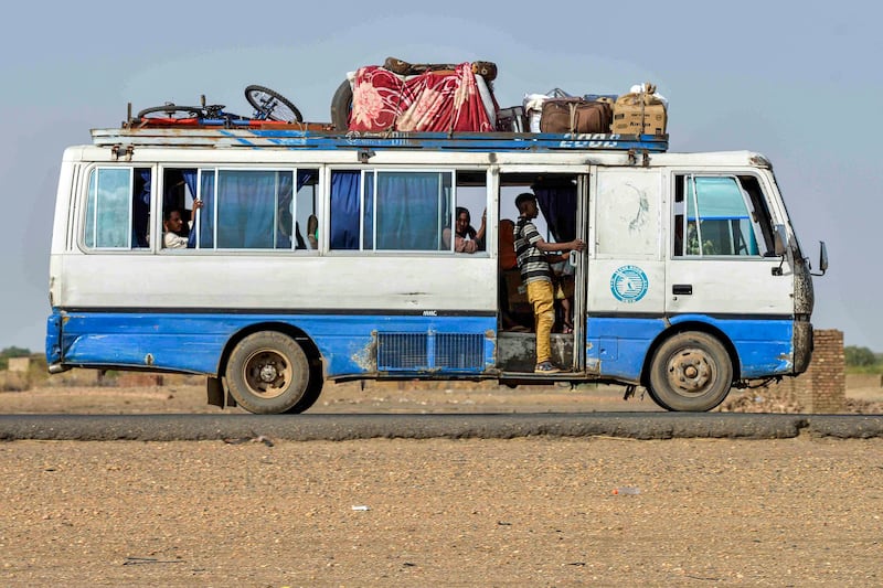 A bus carrying passengers and luggage moves along a road from Khartoum to Wad Madani