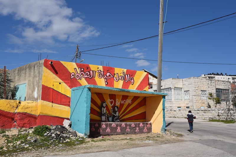 A boy passes a painted bus stop in the West Bank village of Beitin. 