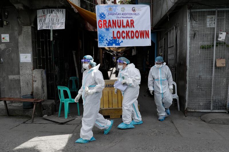 Health workers in protective suits walk after performing swab tests on residents at a village under lockdown in Manila. AP