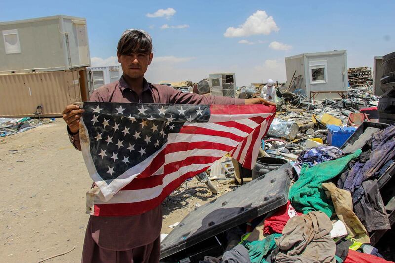 epa09227140 An Afghan man shows a US flag as he visits a junk yard to buy items which were discarded by the US and NATO forces, at a yard in Kandahar, southern Afghanistan, 25 May 2021. As the US and NATO forces withdraw, they destroyed most of the equipment under their use leaving behind decades of war, selling the scrap for millions of dollars to those willing to buy it.  EPA/M. SADIQ