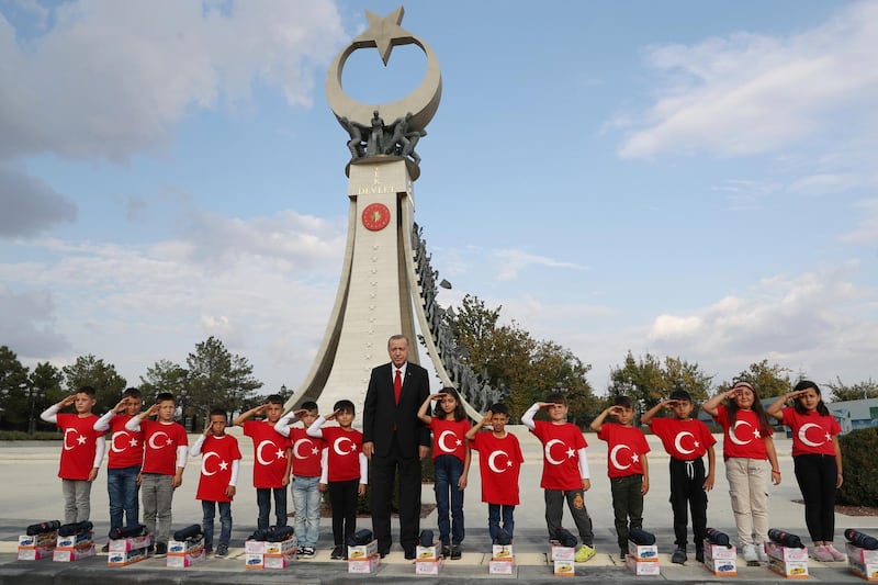 Turkish President Recep Tayyip Erdogan poses for photos with primary school students from a village of Black Sea city of Samsun, who give a military salute outside the presidential palace, in Ankara. Erdogan has responded angrily to widespread criticism in the West of Turkey's incursion in northeast Syria. AP, Pool