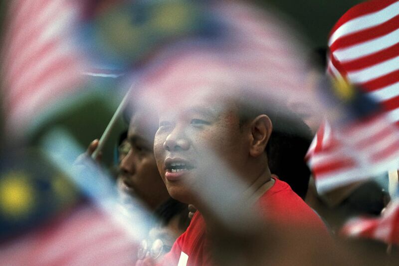 Attendees wave Malaysian flags and sing the anthem during National Day celebrations in Putrajaya, Malaysia. Bloomberg