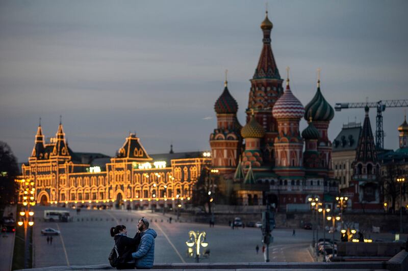 A couple enjoy warm weather on a bridge with St. Basil's Cathedral, right, and an almost empty Red Square after sunset in Moscow, Russia. AP Photo