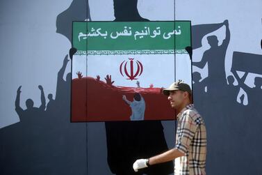 A man walks past a painting on a wall with writing in the Dari Language reading 'We cannot breath' during a protest against 'killings of Afghans in Iran' in Kabul, Afghanistan, on Monday, June 15, 2020. AP