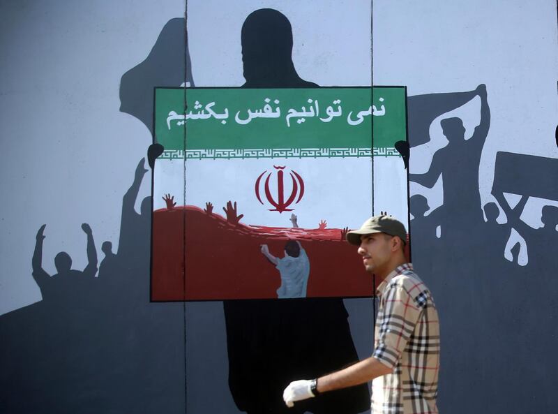 A man walks past a painting on a wall with writing in the Dari Language reading "We cannot breath" during a protest themed Killings of Afghans in Iran in Kabul, Afghanistan, Monday, June 15, 2020. The violent deaths of Afghan refugees inside Iran has sparked an uproar despite denials from Tehran. (AP Photo/ Rahmat Gul)