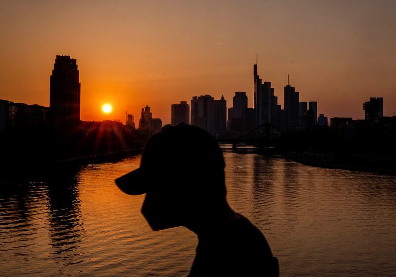 A man wears a face mask as he walks on a bridge over the river Main as the sun sets in Frankfurt, Germany, Thursday, March 24, 2022.  (AP Photo / Michael Probst)