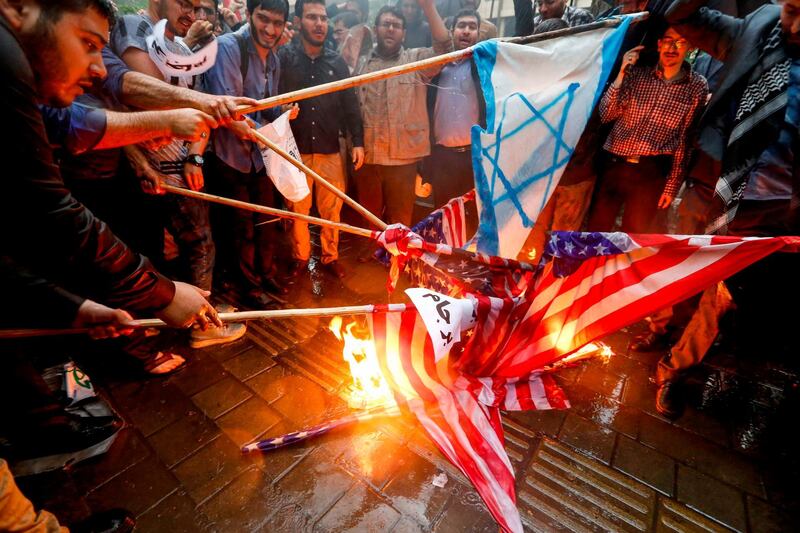 Iranians burn US flags and make-shift Israeli flgas during an anti-US demonstration outside the former US embassy headquarters in the capital Tehran on May 9, 2018.
Iranians reacted with a mix of sadness, resignation and defiance on May 9 to US President Donald Trump's withdrawal from the nuclear deal, with sharp divisions among officials on how best to respond.
For many, Trump's decision on Tuesday to pull out of the landmark nuclear deal marked the final death knell for the hope created when it was signed in 2015 that Iran might finally escape decades of isolation and US hostility.  / AFP PHOTO / ATTA KENARE