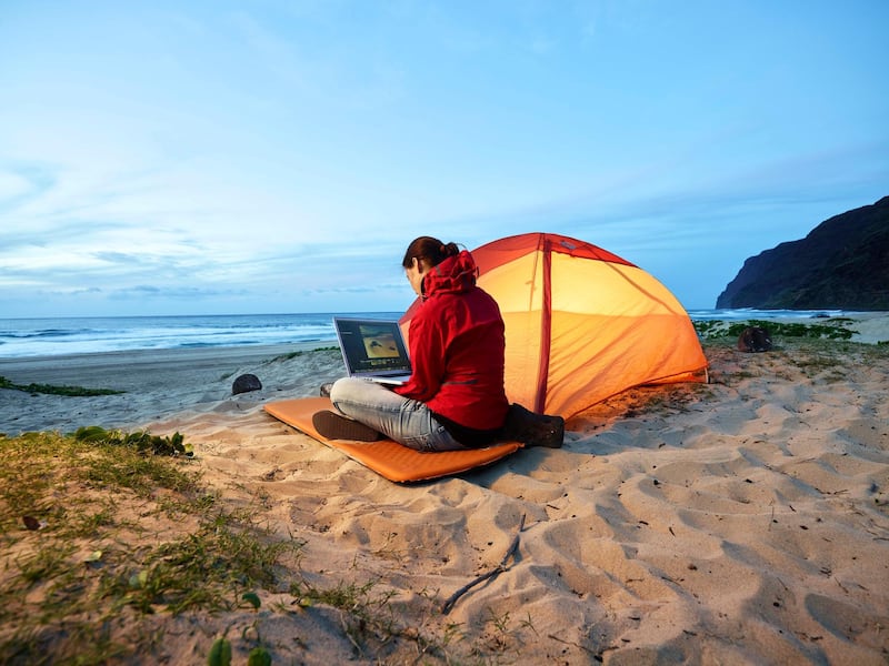 USA, Hawaii, Kauai, Polihale State Park, woman using laptop at tent on the beach at dusk, Getty Images