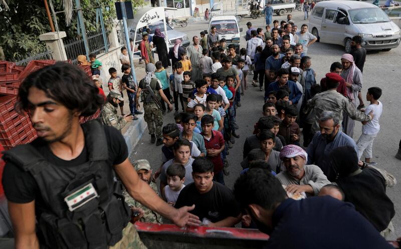 People stand in a queue to receive bread from Turkey-backed Syrian rebel fighters in the border town of Tal Abyad, Syria. REUTERS