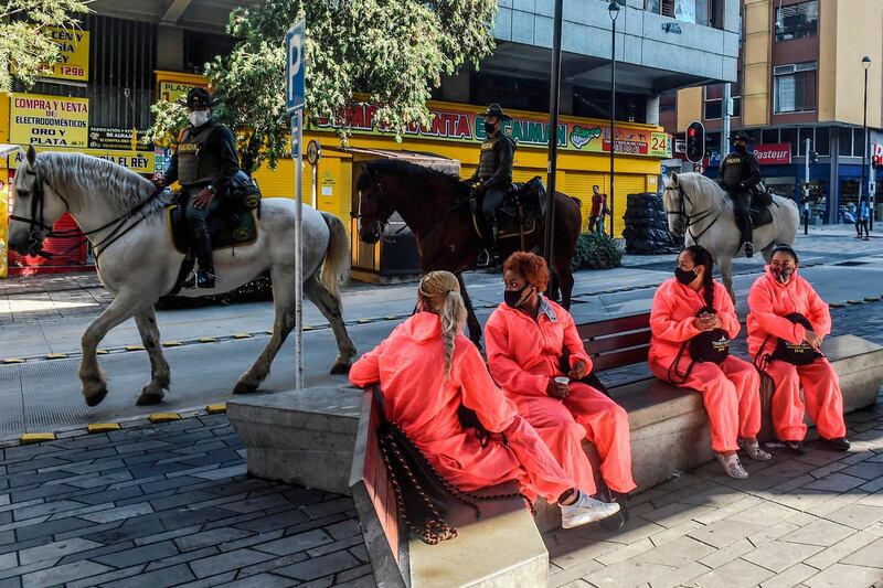 Women wearing personal protective equipment look at mounted police patrolling a street in Medellin in Colombia amid the pandemic.  AFP