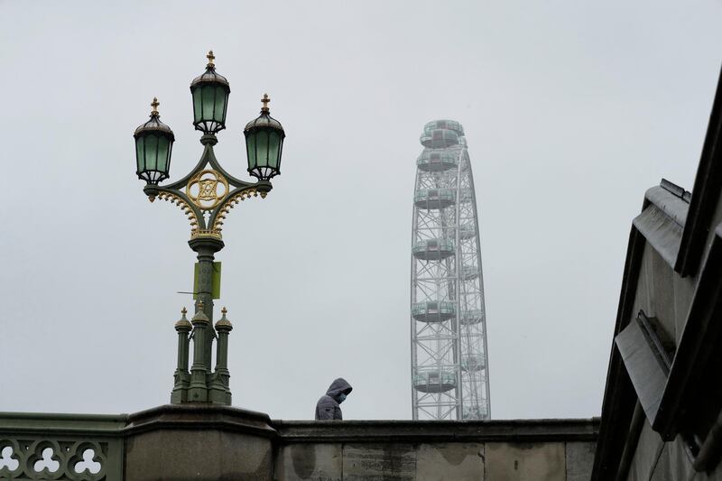 A man wearing a face mask walks over Westminster Bridge on a rainy day in central London. AP Photo