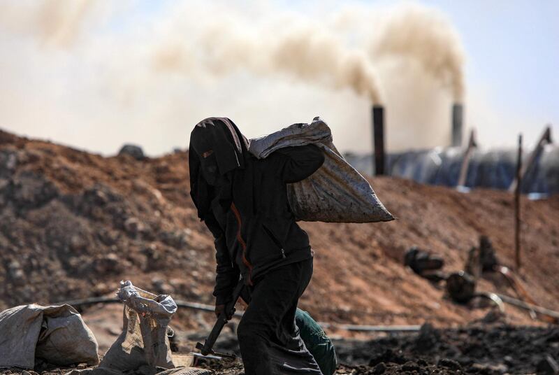 A man labours at a makeshift oil refinery near the village of Tarhin, in Aleppo, Syria, while pollution billows from chimneys in the background. AFP
