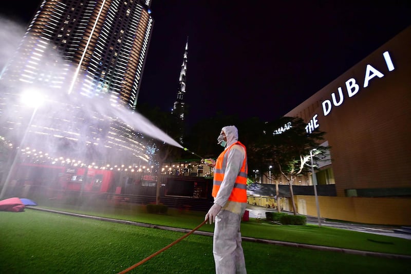 A municipal worker disinfects the streets as a preventive measure against the spread of COVID-19 (novel cornavirus), as the Burj Khalifa is seen in the background, in downtown Dubai, on March 27, 2020. The United Arab Emirates, of which Dubai is a member, has imposed a March 26 to 29 nightime lockdown to allow for outdoors and public transport sanitation operations, amid the outbreak of the new coronavirus. / AFP / GIUSEPPE CACACE
