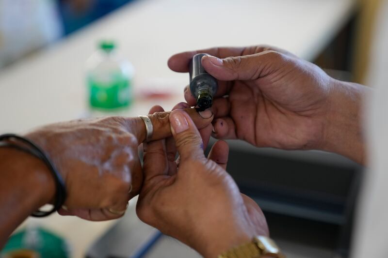 An election worker places ink on the fingers of a man after he finished voting at a polling centre in Quezon City. AP