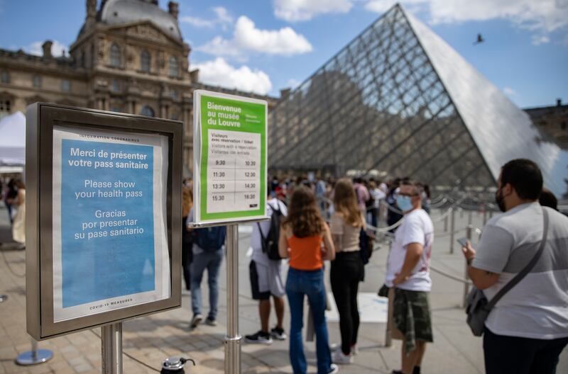 Tourists queue at the Louvre, near a sign saying a vaccine passport is required to enter the museum, on August 5. EPA