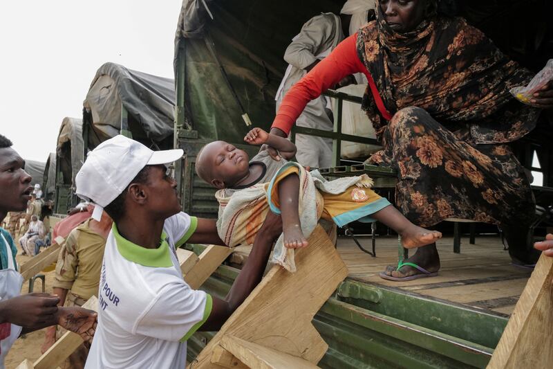 A volunteer hands a child to his mother, a Sudanese woman, in a French Army truck that will relocate them to a refugee camp  in Ourang, Chad.